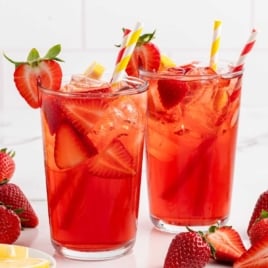 Two tall glasses of strawberry sweet tea with garnishes of fresh lemon and strawberries, surrounded by ingredients.