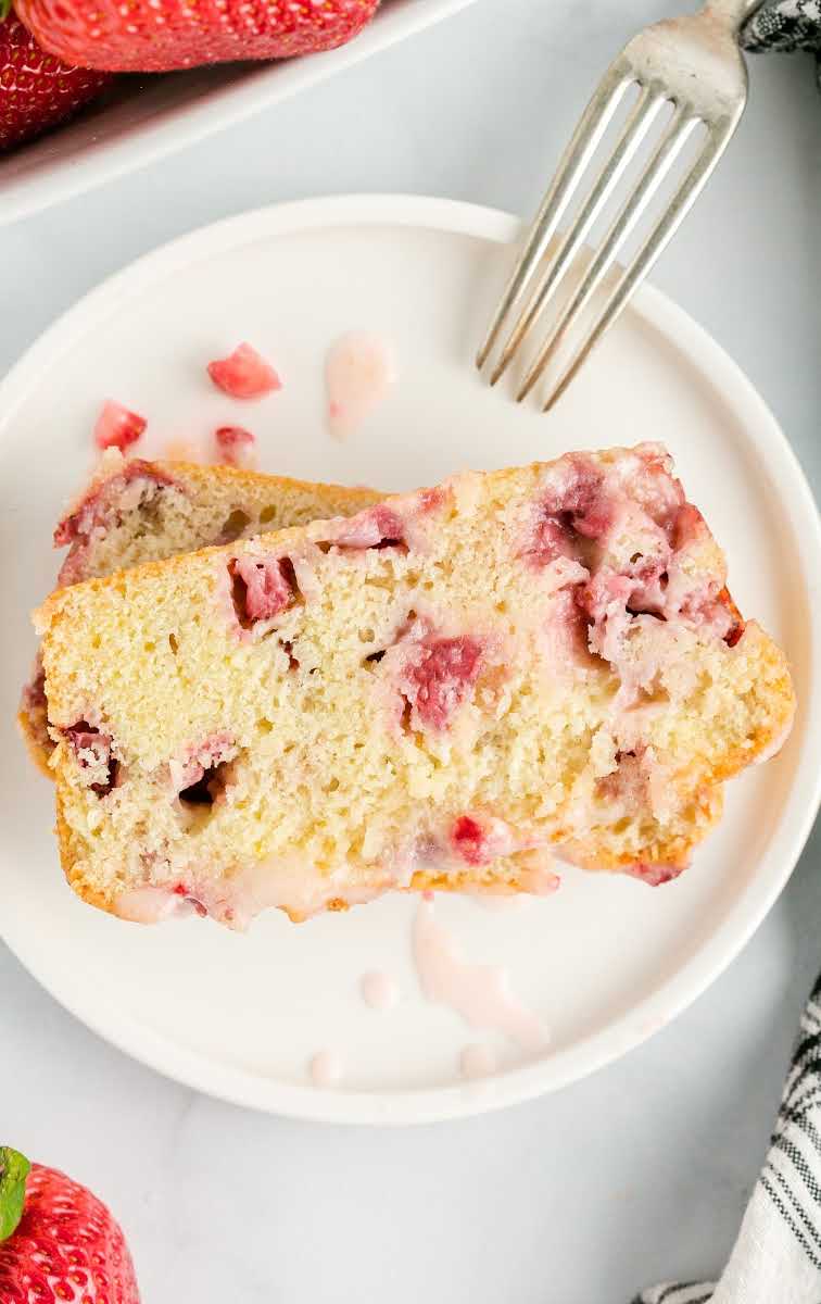 a loaf of strawberry bread with strawberries and glaze on top on a white plate