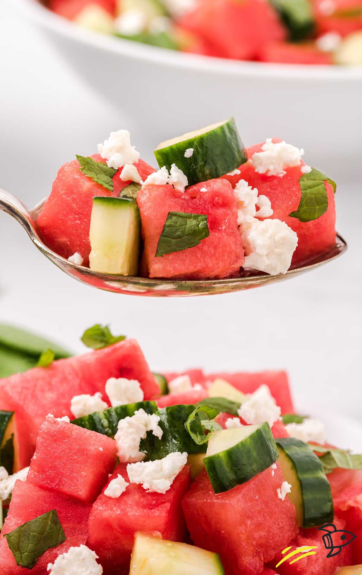 close up shot of watermelon salad topped with mint leaves and feta cheese on a spoon