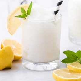 close up shot of alcoholic frozen lemonade in a clear glass with a slice of lemon and mint served with a straw