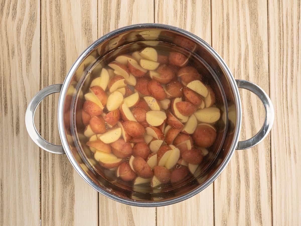 A pot filled with sliced red potatoes soaking in water sits on a light wooden surface, ready to be used in your favorite Chicken Foil Packets recipe.
