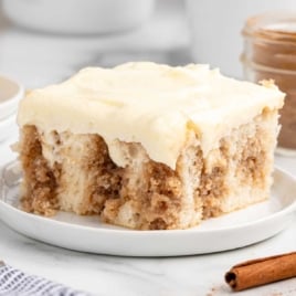 Square slice of cinnamon roll poke cake topped with cream cheese frosting on a plate