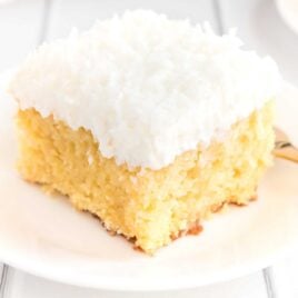 close up shot of coconut poke cake with coconut frosting on a white plate
