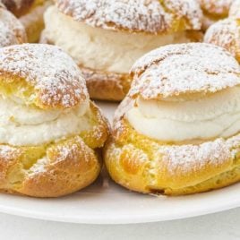 close up shot of cream puffs sprinkled with powdered sugar on a plate