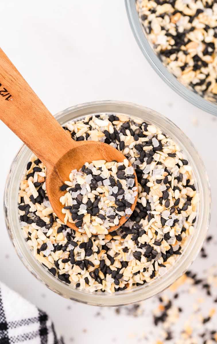 close up overhead shot of everything bagel seasoning in a clear jar with a wooden spoon