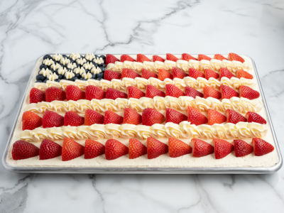 A festive American Flag Cake decorated with sliced strawberries for red stripes, piped white frosting for white stripes, and blueberries with frosted stars creating the blue field—perfect for any patriotic celebration.