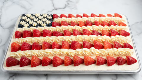 A festive American Flag Cake decorated with sliced strawberries for red stripes, piped white frosting for white stripes, and blueberries with frosted stars creating the blue field—perfect for any patriotic celebration.