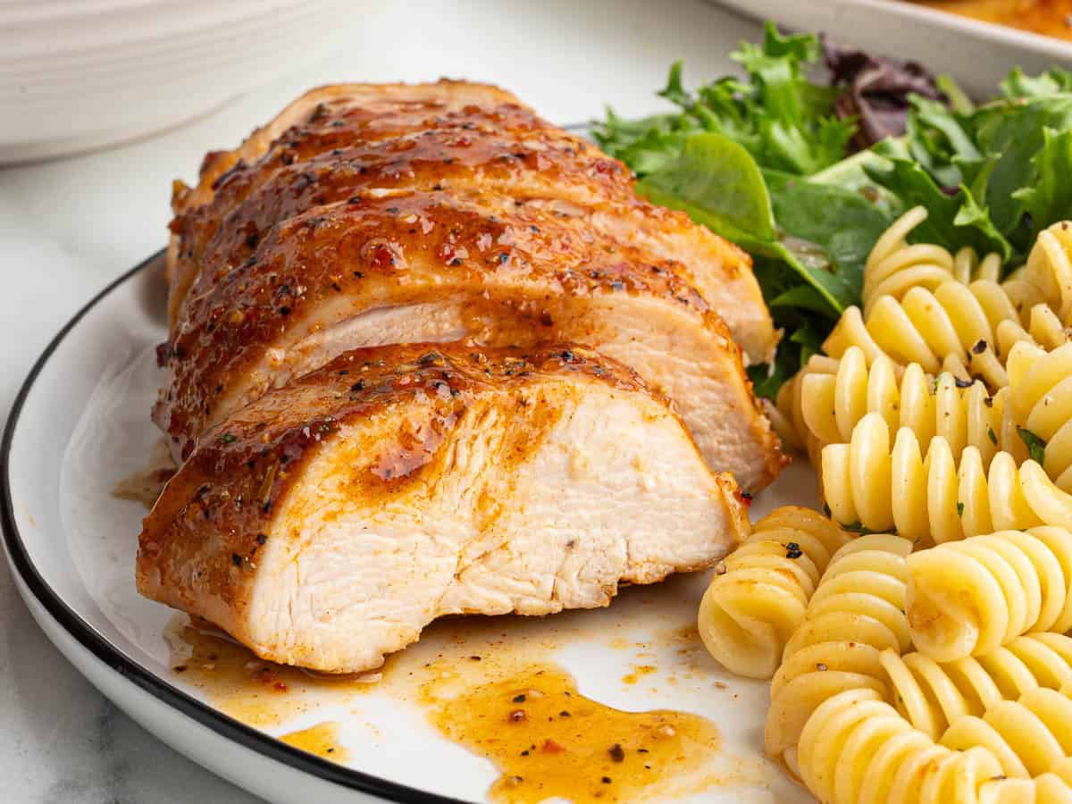 Sliced seasoned chicken breast with sauce, served with cooked rotini pasta and a side of fresh mixed greens on a white plate—an Italian Chicken Recipe perfect for any occasion.