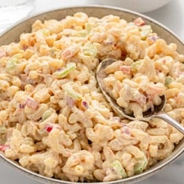 Overhead view of a large bowl of creamy macaroni salad with vegetables and a spoon ready for serving.