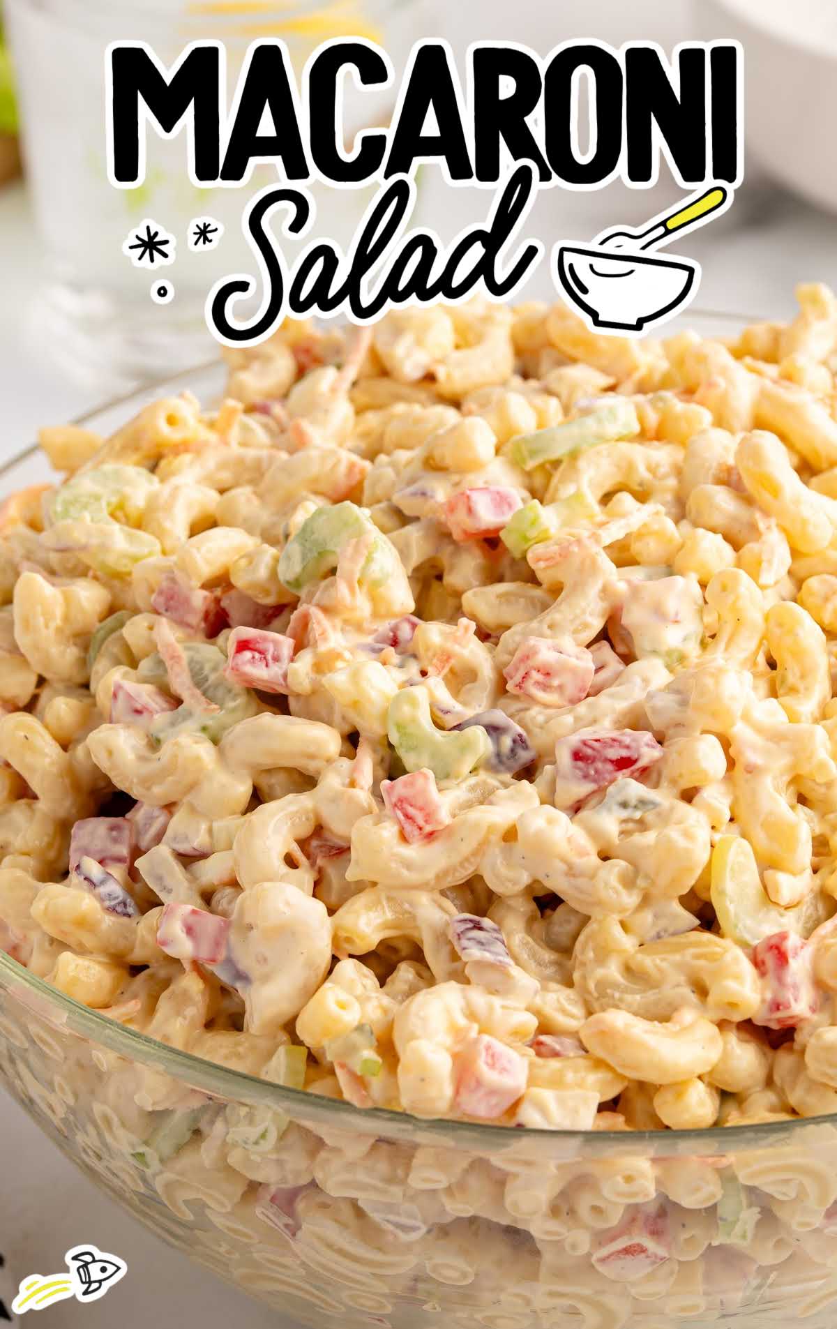 Glass bowl filled with classic macaroni salad with diced vegetables and thick creamy dressing.