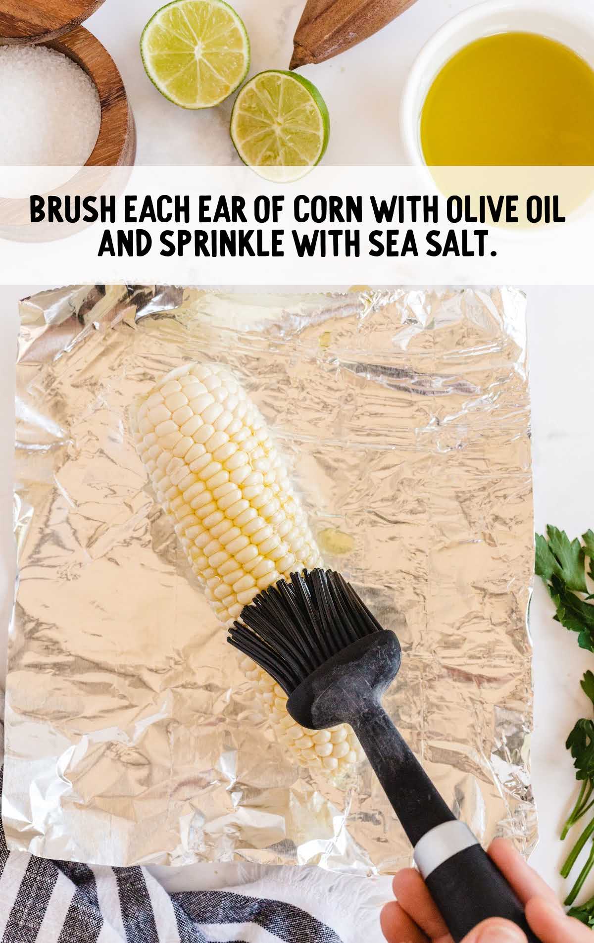 corn being brushed with olive oil on aluminum foil