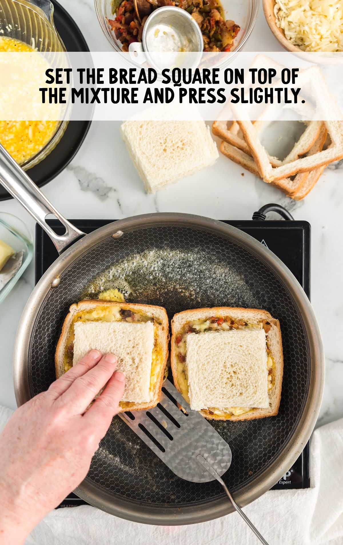 Placing the removed bread square on top of the filled bread on a skillet, pressing slightly.