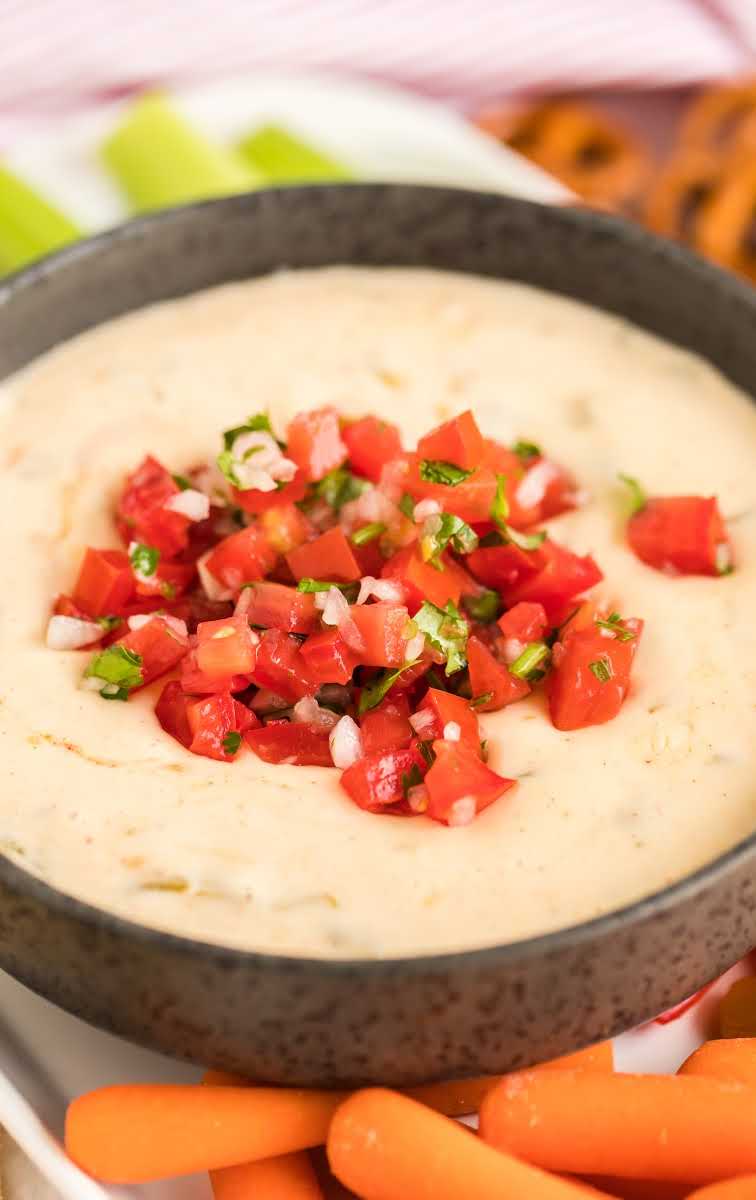 close up shot of a bowl of white queso dip topped with diced tomatoes
