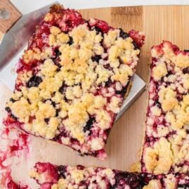 close up shot of Blackberry Pie Bars stacked on top of each other on a plate with blackberries