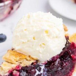 a slice of Blueberry Pie on a plate topped with vanilla ice cream
