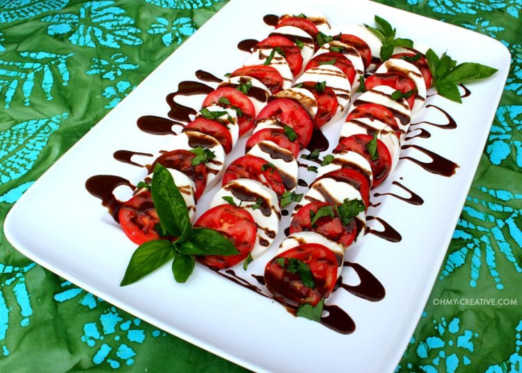 white square plate with mozzarella cheese, tomatoes, basil and glaze drizzled on top