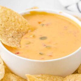 close up shot of a bowl of Cheese Dip with a tortilla chip dipped into it
