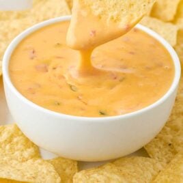 close up shot of a bowl of Cheese Dip with a tortilla chip being dipped into it