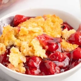 Close-up of a spoonful of cherry dump cake in a white bowl with a glass of milk in the background.