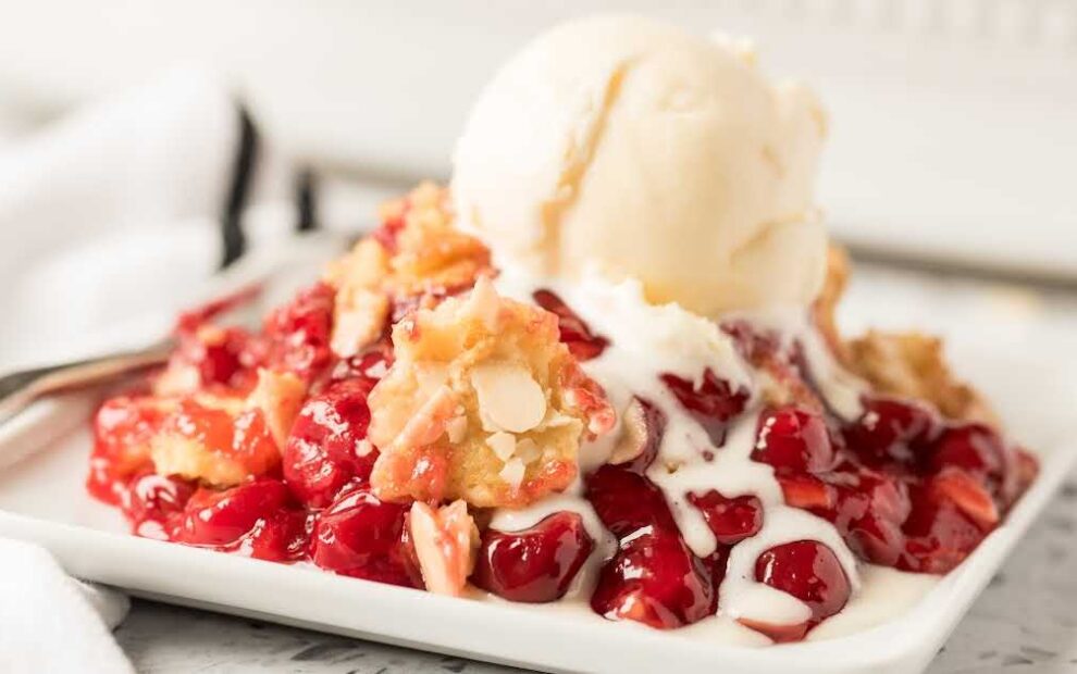 close up shot of a serving of cherry dump cake topped with vanilla ice cream on a plate