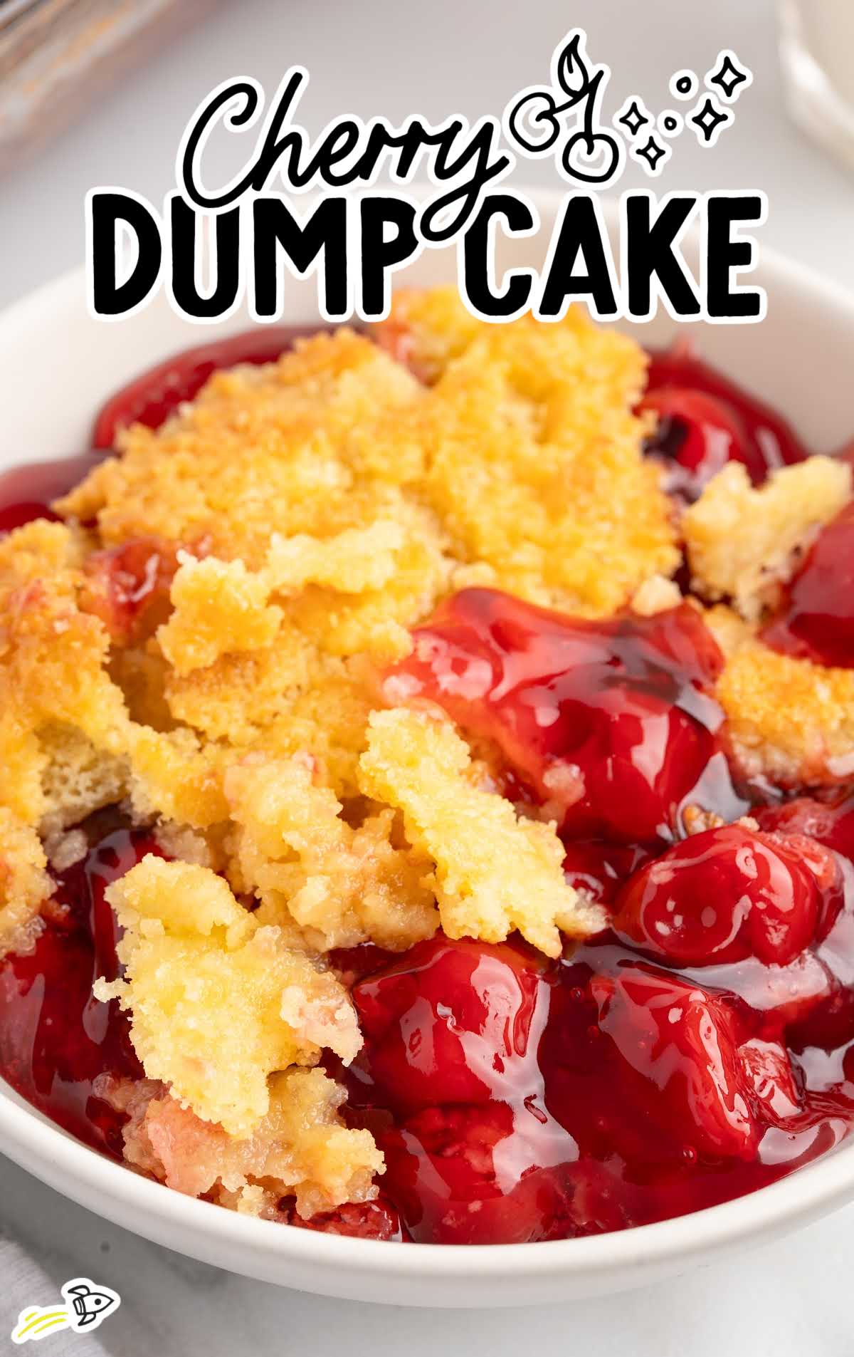 Overhead view of cherry dump cake in a white bowl showing golden cake topping and glossy cherry filling.