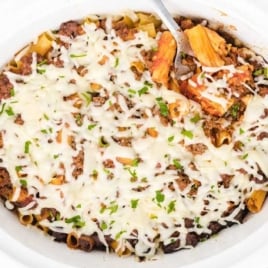 Overhead view of crockpot baked ziti topped with melted mozzarella and chopped parsley.