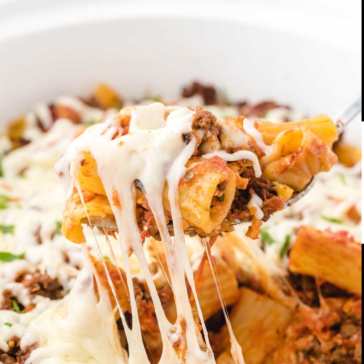 Close-up of cheesy baked ziti on a serving spoon with mozzarella stretching.