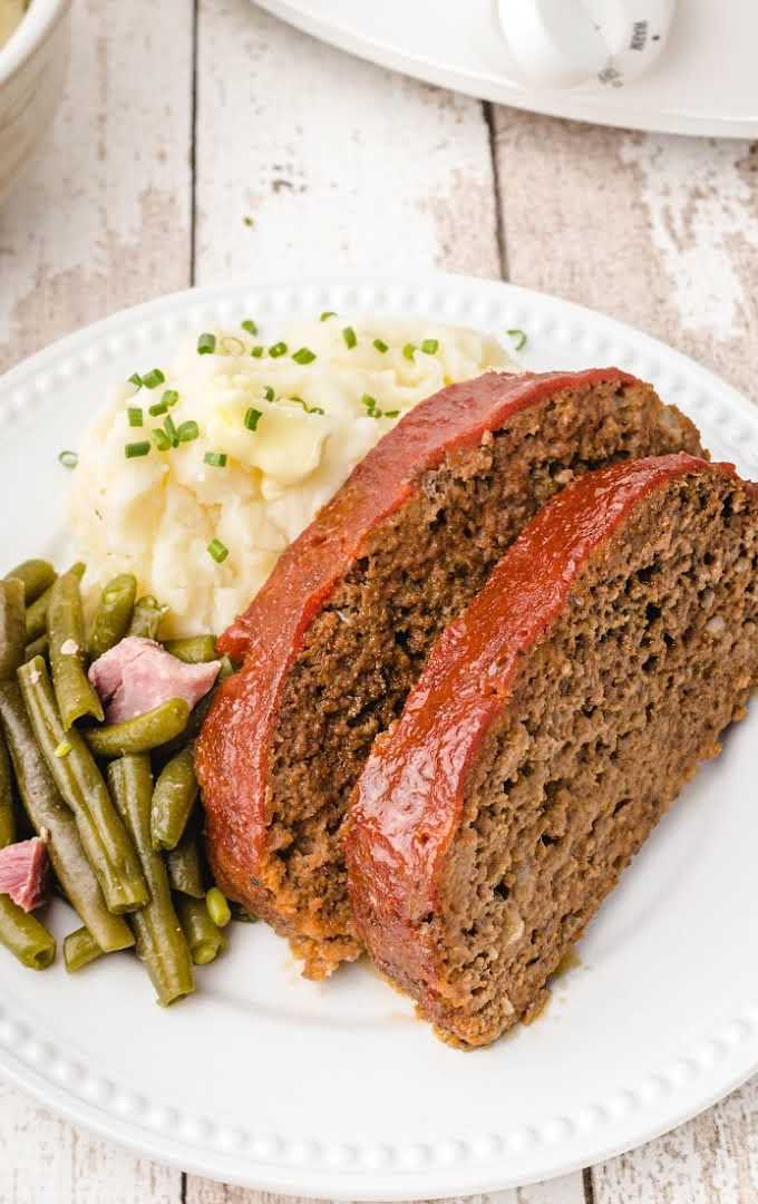 close up overhead shot of slices of crockpot meatloaf served on a plate with mashed potatoes and green beans