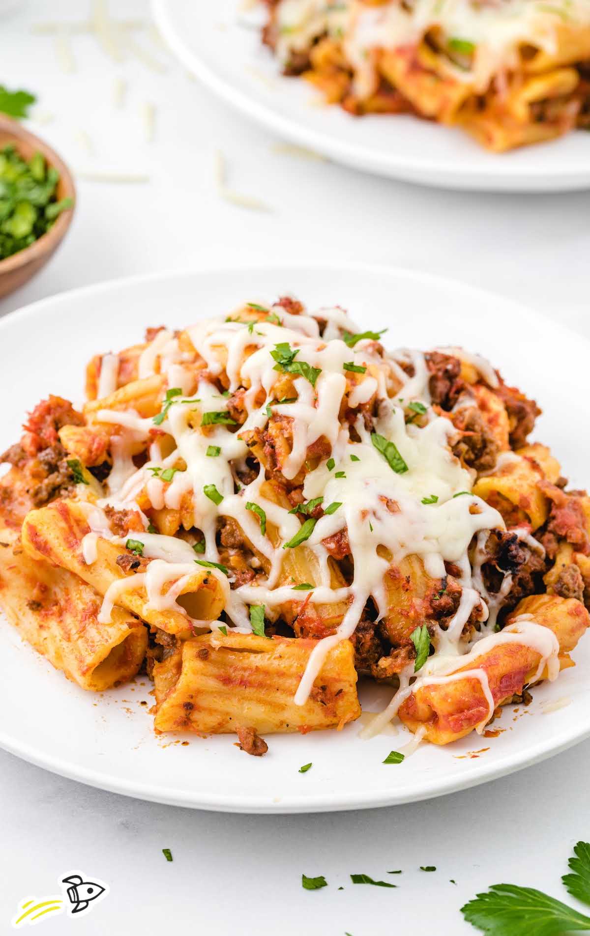 Plate of crockpot baked ziti garnished with melted cheese and chopped parsley.
