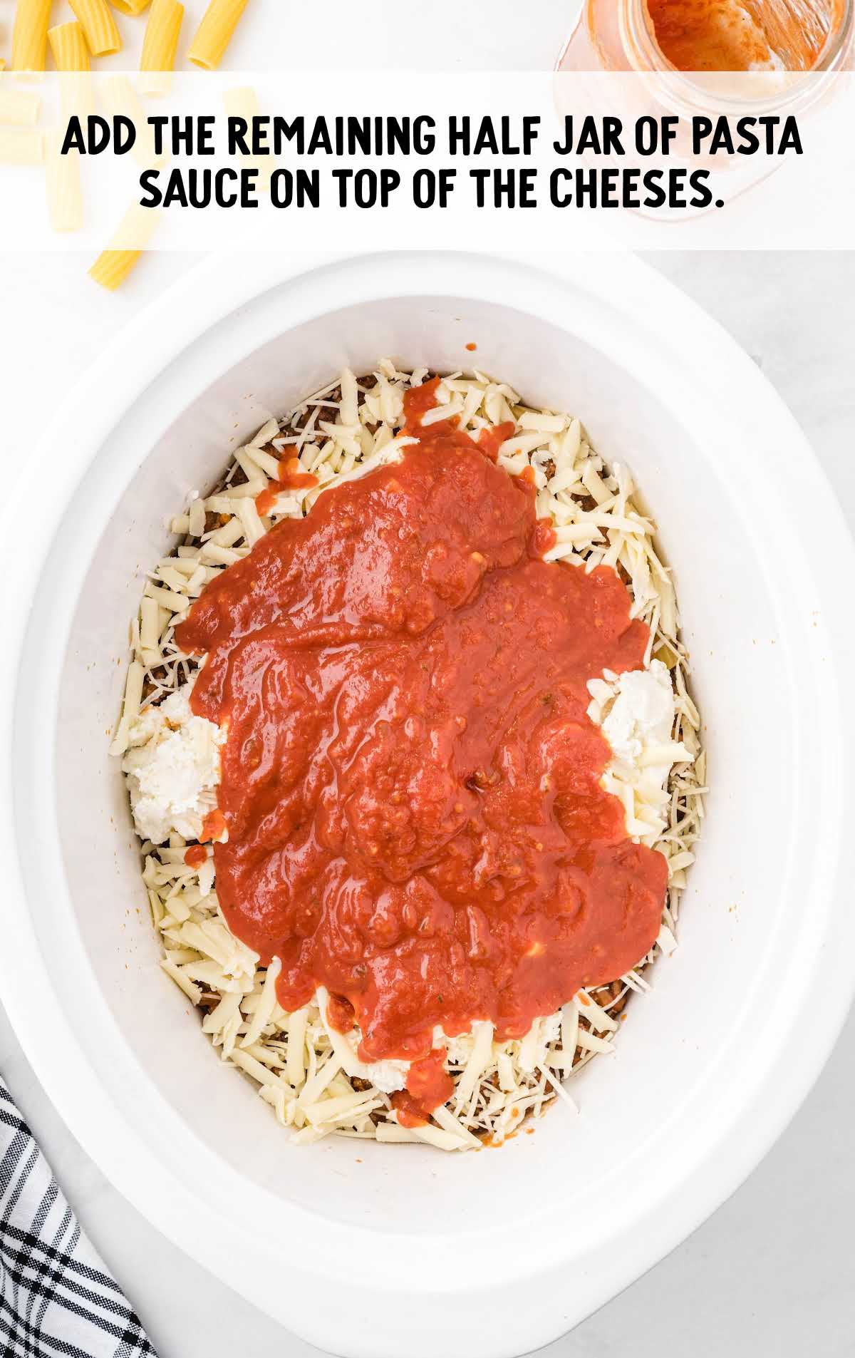 Overhead image of shredded cheese and pasta sauce layered inside a crockpot.