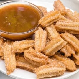 close up shot of a bunch Disney Churros on a plate with a bowl of dipping sauce