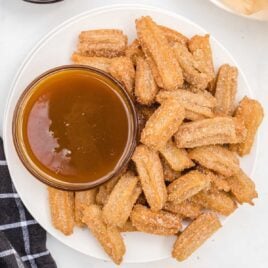 close up overhead shot of a bunch Disney Churros on a plate with a bowl of dipping sauce