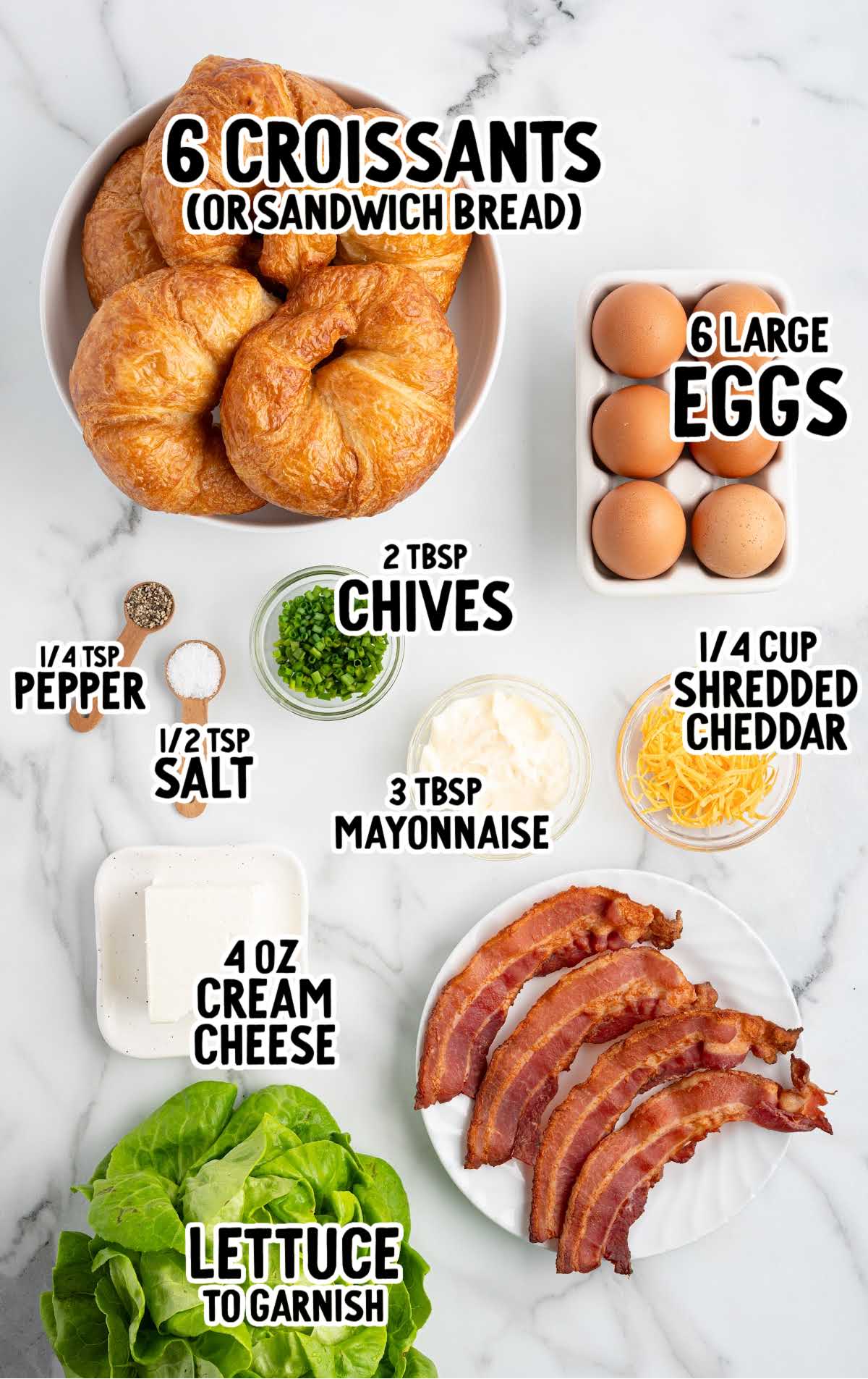 Overhead view of labeled egg salad sandwich ingredients including croissants, eggs, bacon, cheese, cream cheese, and lettuce.