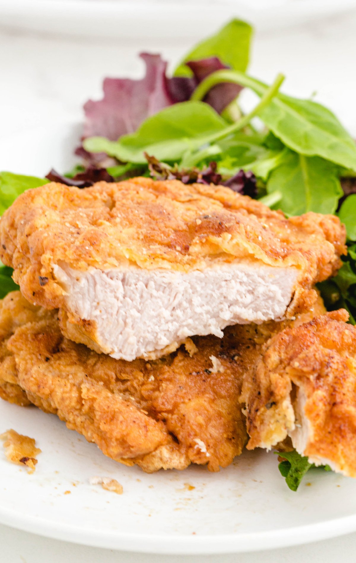 two fried pork chops on a plate with a bite take out of one of the pork chops