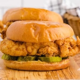 Two crispy fried chicken sandwiches with pickles on toasted brioche buns served on a wooden board