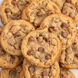 Plate stacked with golden-brown gluten-free chocolate chip cookies, topped with melty chocolate chips, and bold text overlay reading “Gluten-Free Chocolate Chip Cookies – Soft & Gooey!”