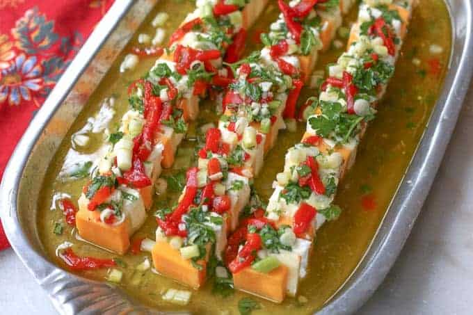 silver tray filled with marinade liquid and a mixture of cheeses topped with fresh herbs