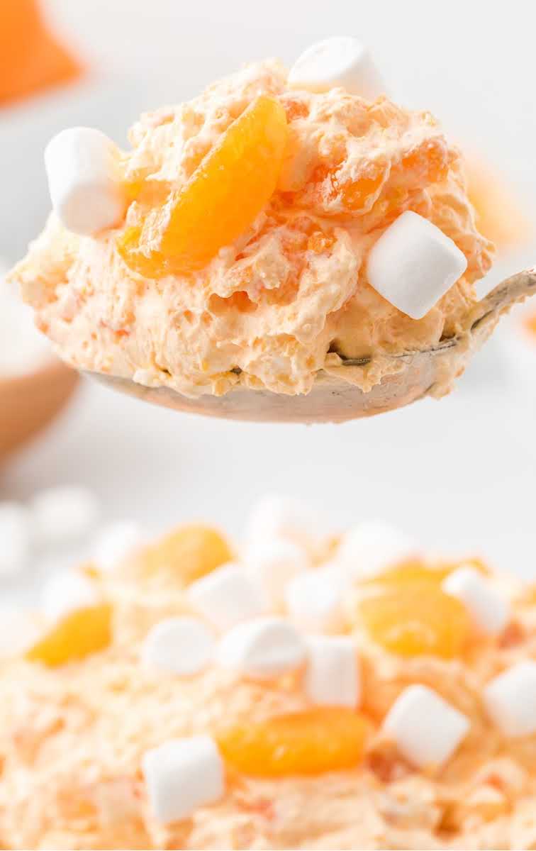 close up shot of a spoonful of orange creamsicle salad topped with mandarin oranges and mini marshmallows