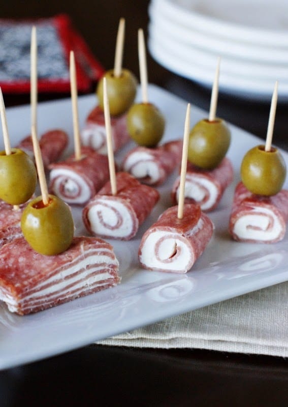 white plate with salami and cream cheese rolled up into bites with a toothpick  and olive