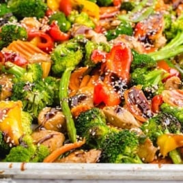 Side angle of roasted sheet pan stir fry with vegetables and chicken, topped with sesame seeds and sauce.