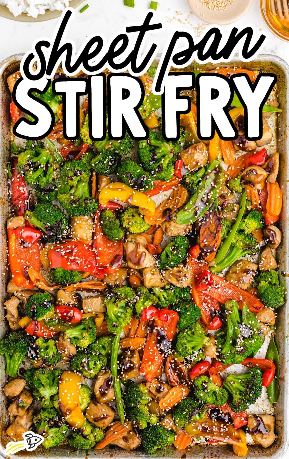 Overhead view of colorful sheet pan stir fry with broccoli, peppers, chicken, and sesame seeds on a baking tray.