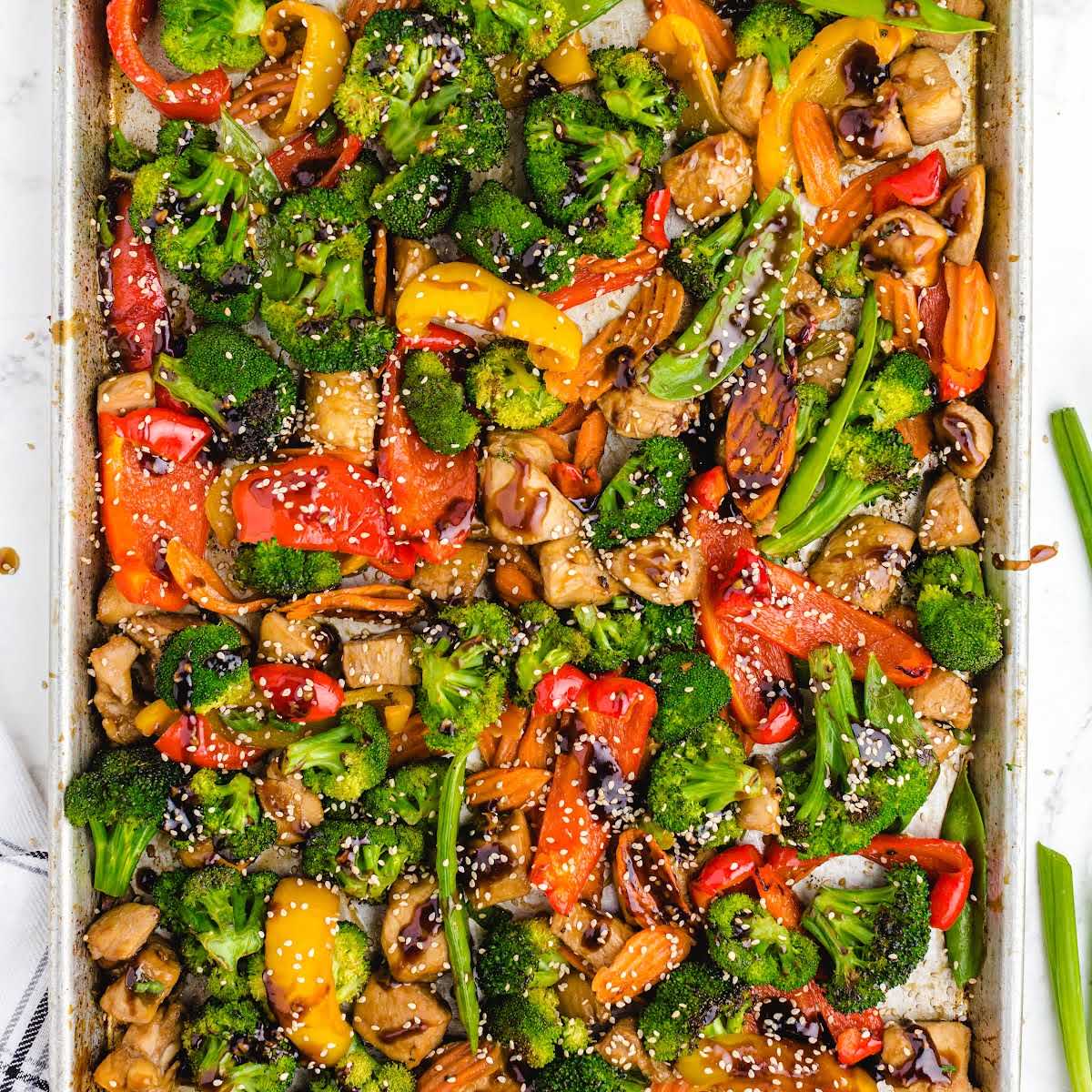Full pan of sheet pan stir fry filled with cooked chicken, broccoli, peppers, carrots, and sesame seeds.