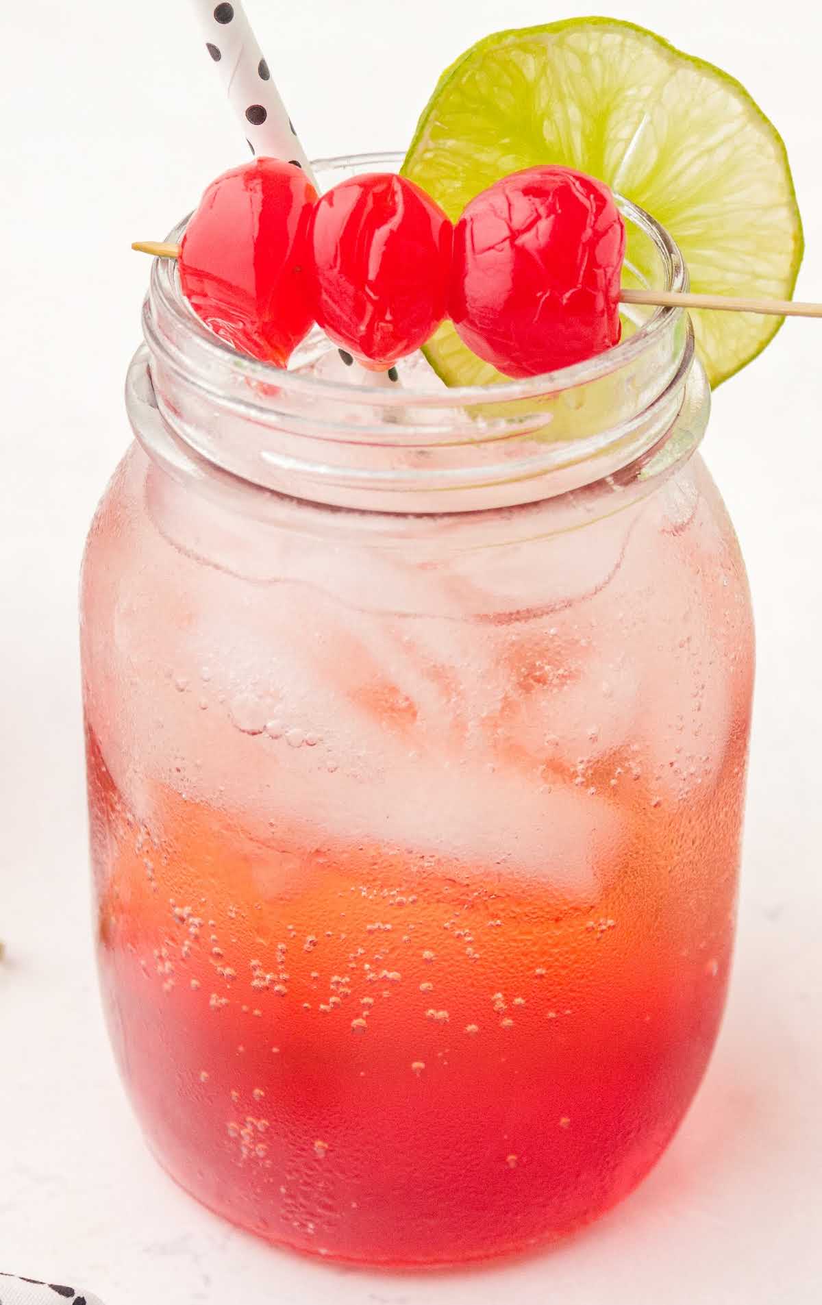 close up shot of a glass of Shirley Temple garnished with cherries and lime slices