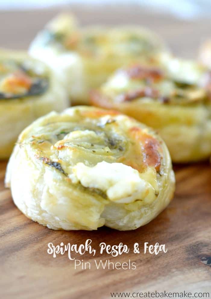 pastry filled with spinach, pesto and feta, rolled up into a log and sliced into pinwheels and sitting on a wood board