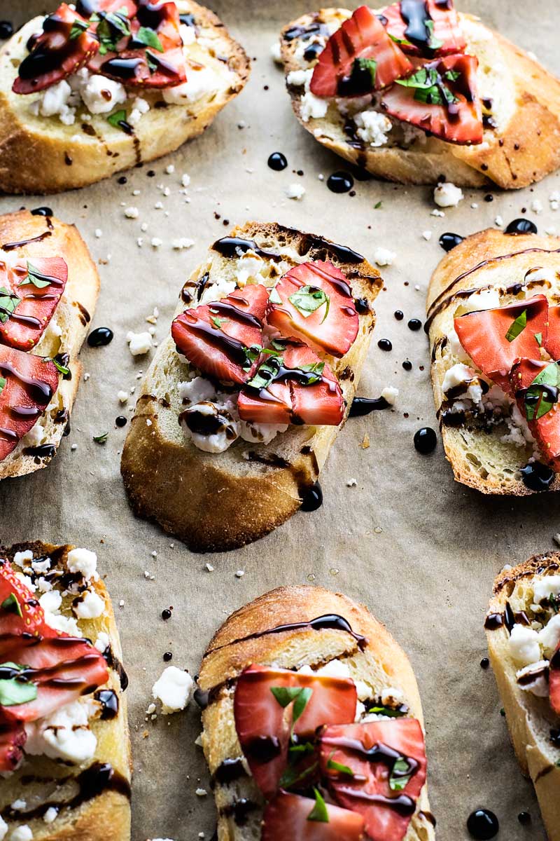 ovals of toast with cheese, strawberries and glaze drizzled on top.