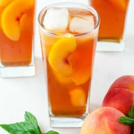 a tall glass of Sweet Peach Iced Tea served with peaches and a mint