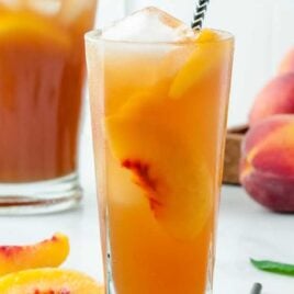 a tall glass of Sweet Peach Iced Tea served with peaches and a mint