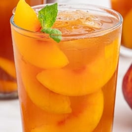 Text overlay “Vintage Homemade Sweet Peach Iced Tea” on close-up of iced tea with peach slices and mint garnish.
