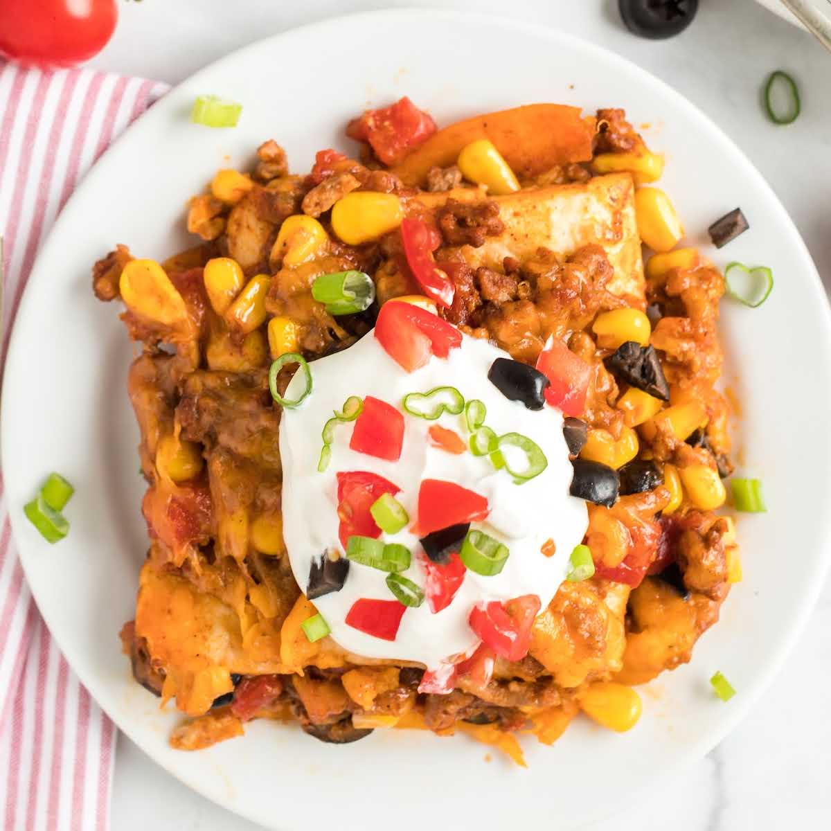 close up overhead shot of a plate of taco bake topped with sour cream, tomatoes, and green onions