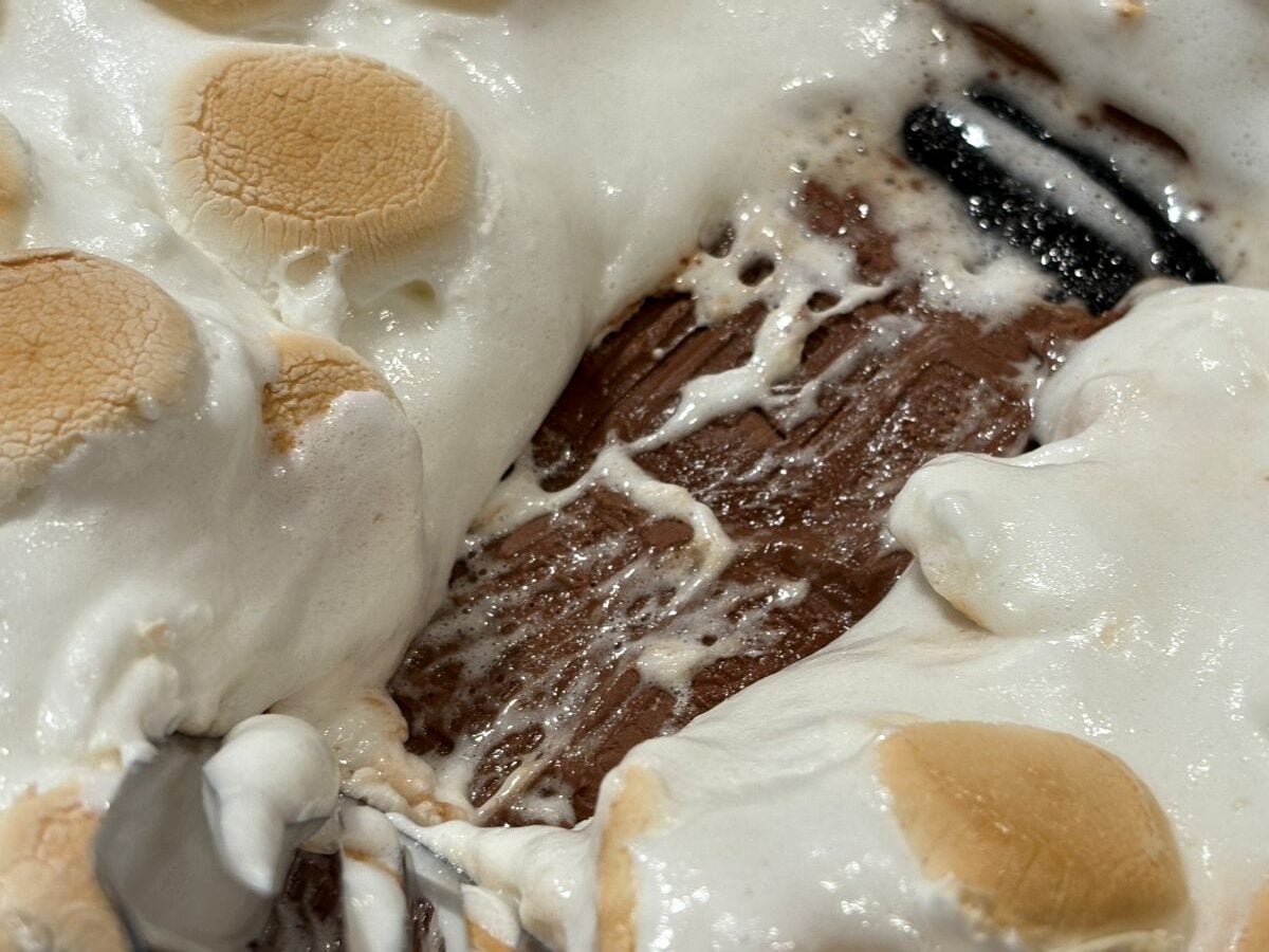 Close-up of toasted marshmallows melted over a layer of chocolate, with gooey textures visible and a spoon partially in view, capturing the irresistible appeal of this S'mores Dip Recipe.